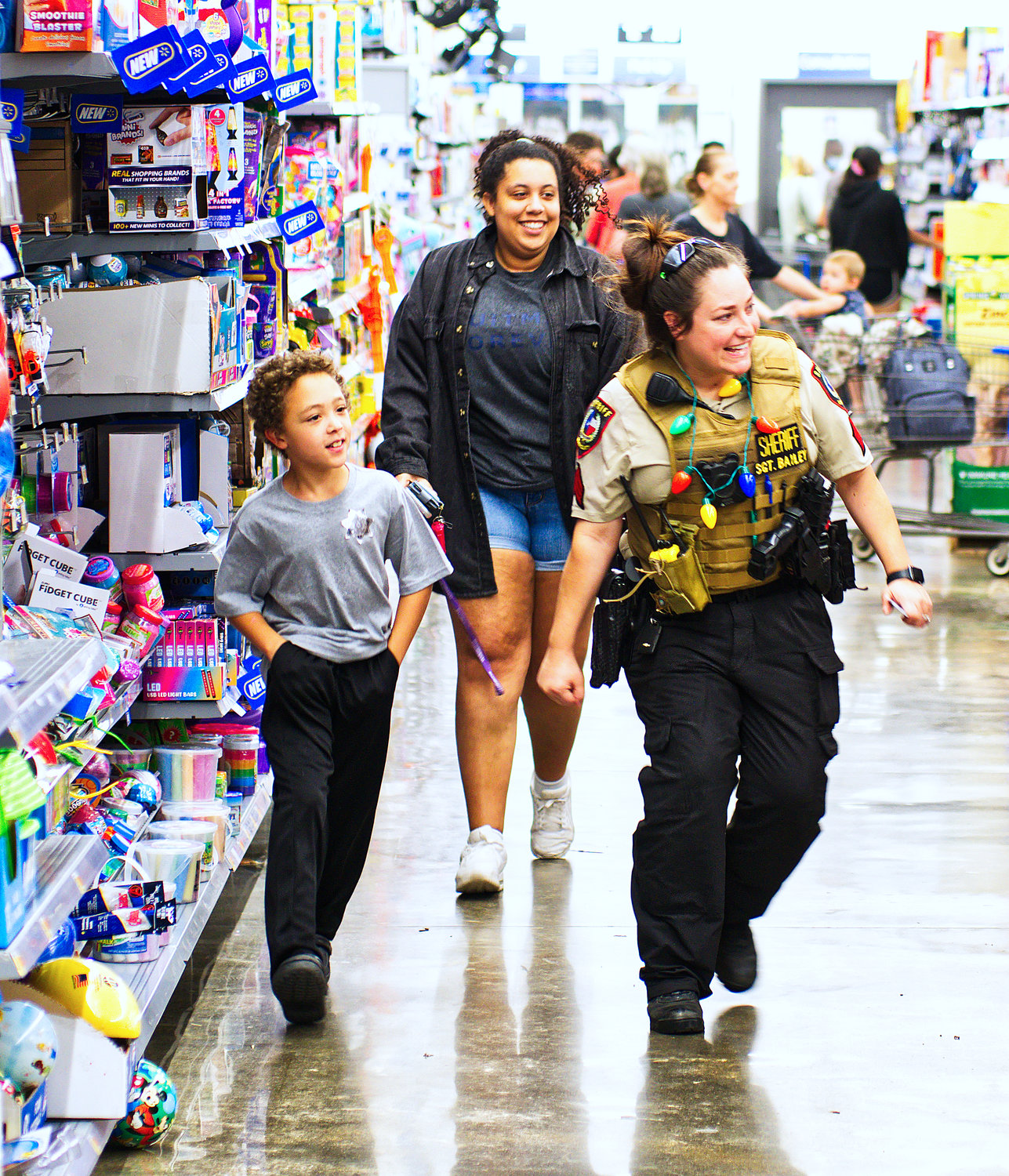 Wood County Sheriff’s Department Sgt. Heather Bailey helps Keelan Sanders locate items at Walmart during the Blue Santa shopping event last Wednesday. Local law enforcement officers assisted 50 children with more than $200 each in gifts and items they selected.
